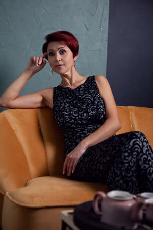 a woman in an elegant dress is sitting on a bright yellow sofa. Fashion photo