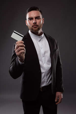 An elegant man with a beard is holding a credit card. Photo on a dark backgroundの写真素材