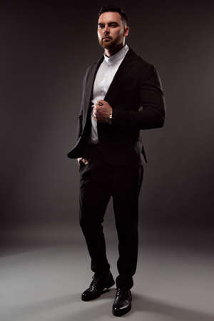 Portrait of a brutal unshaven businessman dressed in a black suit and white shirt posing on a dark background. Close-up photoの写真素材