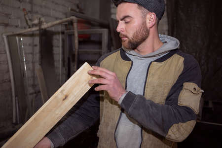 A male carpenter inspects the correct geometry of a wooden Board. Photo of a working carpenter in the carpentry industryの写真素材