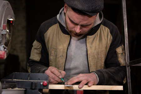 the carpenter's rough hands draw a line on a wooden Board with a pencil and a square. Close-up photo