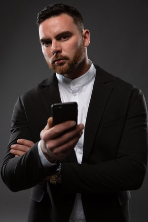 Close-up portrait of a businessman checking messages on his mobile phone. Vertical format on a dark background.の写真素材