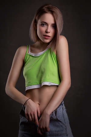 Gorgeous sexy blonde girl in a crop top and unbuttoned jeans poses on a dark background looking at the cameraの写真素材