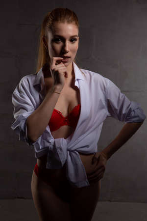 a sexy blonde girl in lacy red underwear poses on a dark background. A girl with a beautiful figureの写真素材
