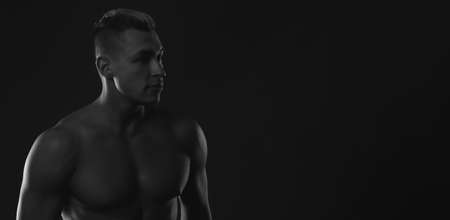 Black and white photo of a strong muscular man with a naked torso on a black background. a place for...