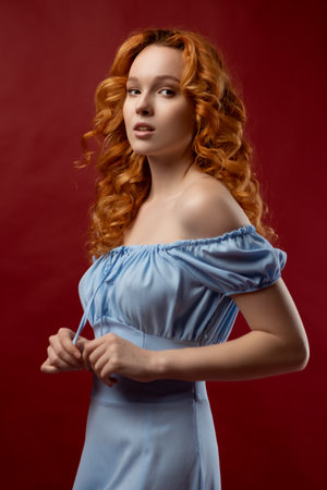 Portrait of a sexy red-haired woman with long hair on a red background. The perfect girl with blue eyes, beautiful clear skin, beautiful natural makeup, red hairの写真素材