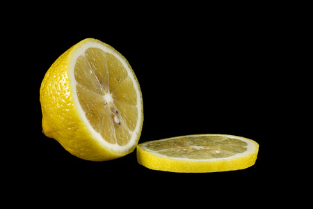 A half and slice of a yellow lemon on a black backgroundの写真素材