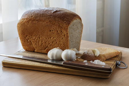 Fresh bread, knife and garlic on the wooden desktop
