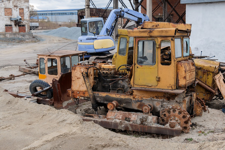The old rusty bulldozer and the working excavator on a dump