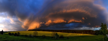 quickly and dramatically evolving the cloudy formation lit by the setting sun over the meadow and a field with blooming rape fieldの写真素材