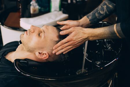 Profile view of bearded man getting his hair washed and his head massaged in hair salon. Cleaning head barber's. Barber men washing client's hair in barbershop or beaty salon.の写真素材