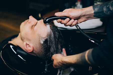 Profile view of bearded man getting his hair washed and his head massaged in hair salon. Cleaning head barber's. Barber men washing client's hair in barbershop or beaty salon.の写真素材