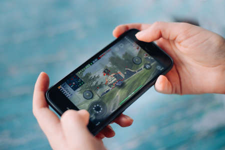 SAINT PETERSBURG, RUSSIA - MAY 27, 2020: Black iPhone in the hands. On-screen game World of Tanks....