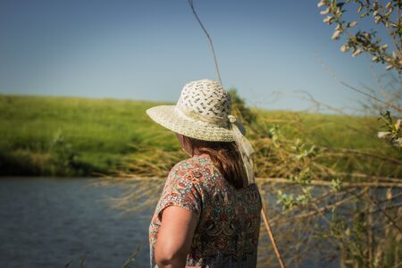 girl in a hat fishing with a rod on the pondの写真素材
