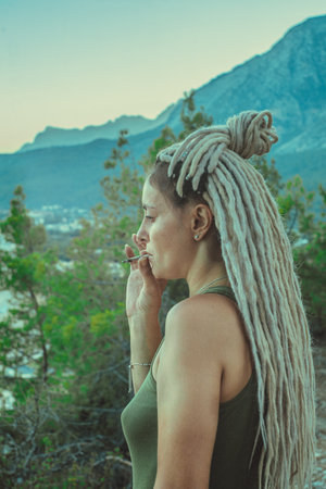 Rastafarian girl with dreadlocks smokes in the mountains.