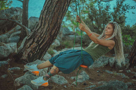 Rasta girl with dreadlocks is resting on the Mediterranean coast on a swing.の写真素材