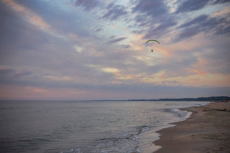 A paraglider flies over the Baltic beach in the evening.
