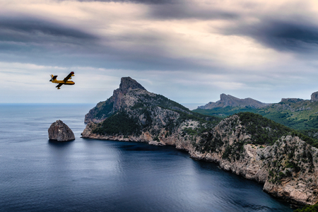 Firefighter plane flying over a beautiful seaside cliffs scenery at Cap de Formentorの写真素材