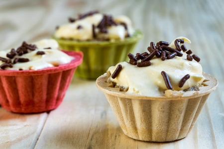 Colorful vanilla cream cupcakes with chocolate granules on a wooden tableの写真素材