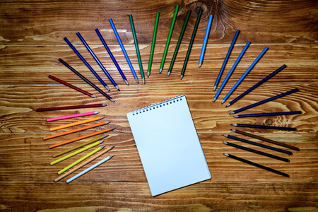 Empty notebook with color pencils around on the wooden tableの写真素材