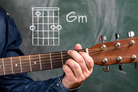 Man in a blue denim shirt playing guitar chords displayed on a blackboard, Chord Gmの写真素材