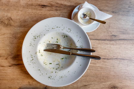 Empty plate with fork and food remnants after meal on a wooden tableの写真素材