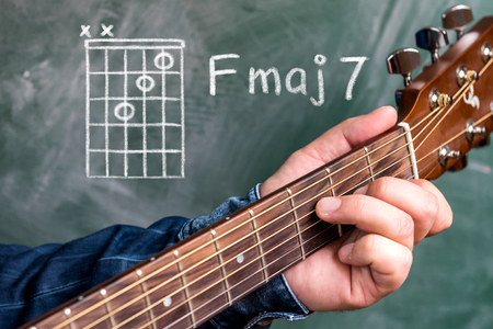 Man in a blue denim shirt playing guitar chords displayed on a blackboard, Chord F major 7の写真素材
