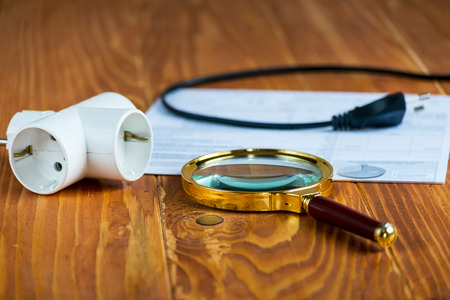Electricity Bill on a wooden table with magnifier and Electric Splitter