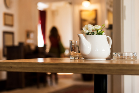 Indoor Restaurant Decoration with Ceramic Milk Pot with Flowers on a Wooden table with a gallery in the backgroundの写真素材