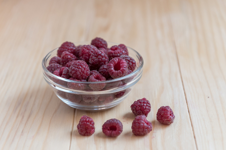 Fresh organic raspberries in a glass bowl on wooden tableの写真素材