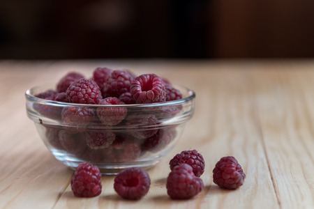 Fresh organic raspberries in a glass bowl on wooden tableの写真素材