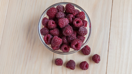 Fresh organic raspberries in a glass bowl on wooden tableの写真素材