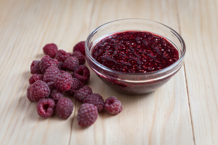 Homemade Raspberry jam in a glass bowl with fresh ripe organic Raspberries on a wooden table