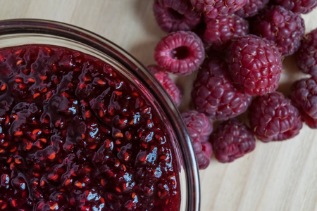 Homemade Raspberry jam in a glass bowl with fresh ripe organic Raspberries on a wooden table