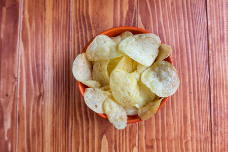 Crispy potato chips in a bowl on wooden background