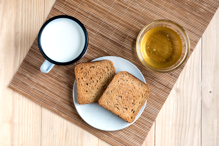 Two Slices of Toast Bread with Tin Mug of Milk and Jar of Honey on a Wooden Table Setupの写真素材