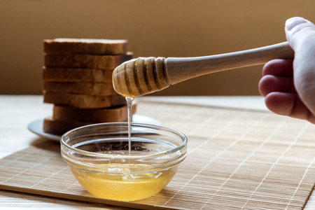 Jar of Honey with Honey Dipper with Toast Bread In the Background on a Wooden Table Setupの写真素材