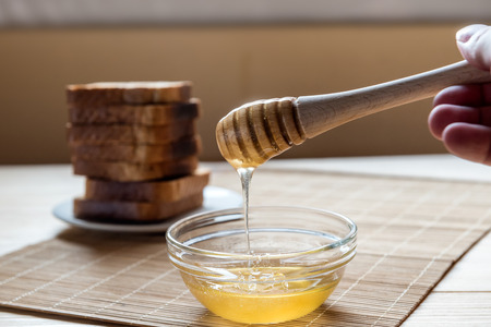 Jar of Honey with Honey Dipper with Toast Bread In the Background on a Wooden Table Setupの写真素材