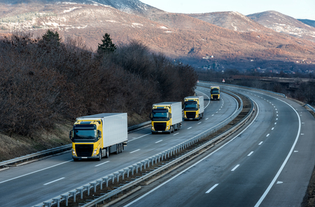 Caravan or convoy of Yellow lorry trucks on country highway under a dramatic skyの写真素材