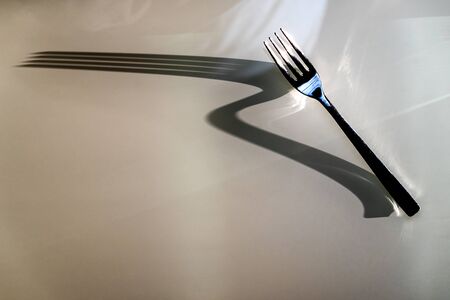 Dinner Fork throws large elongate Shadow on glass table background. Concept of Shadow and Light