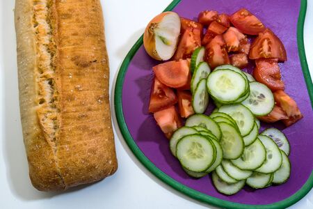 Fresh vegetables chopped in a cutting board - Salad ingredients - cucumber, tomatoes, cherry tomatoes, onion, loaf of breadの写真素材