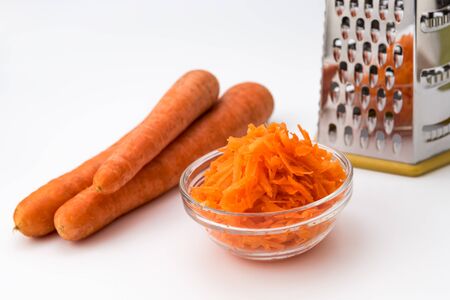 Fresh Grated carrot in a bowl and layout of carrots and grater isolated on white backgroundの写真素材