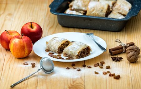 Apple roll pie - Apple Strudel. Pie with apples, cinnamon, walnuts and raisins, sprinkled with powdered sugar in a plate on a wooden tableの写真素材