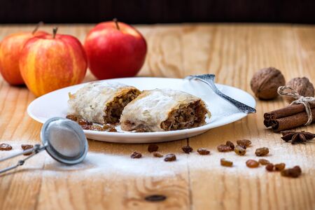 Apple roll pie - Apple Strudel. Pie with apples, cinnamon, walnuts and raisins, sprinkled with powdered sugar in a plate on a wooden tableの写真素材