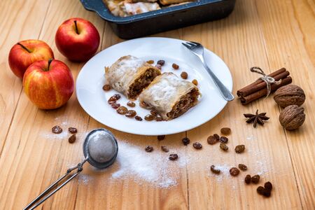 Apple roll pie - Apple Strudel. Pie with apples, cinnamon, walnuts and raisins, sprinkled with powdered sugar in a plate on a wooden tableの写真素材