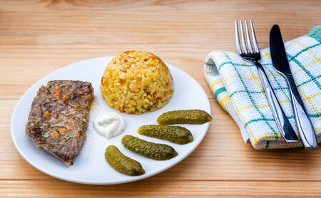 Prepared beef steak with rice risotto, pickles and sauce on white plate on wooden table backgroundの写真素材