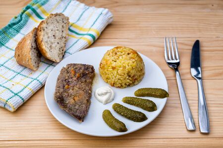Prepared beef steak with rice risotto, pickles and sauce on white plate on wooden table backgroundの写真素材