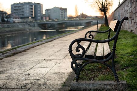 Bench at the promenade by the river bank in the autumn sunset and with soft focused backgroundの写真素材