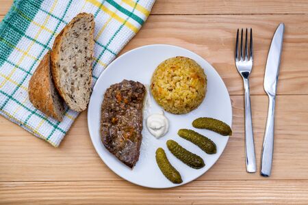 Prepared beef steak with rice risotto, pickles and sauce on white plate on wooden table backgroundの写真素材