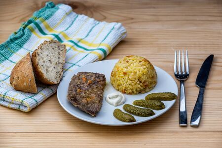 Prepared beef steak with rice risotto, pickles and sauce on white plate on wooden table backgroundの写真素材